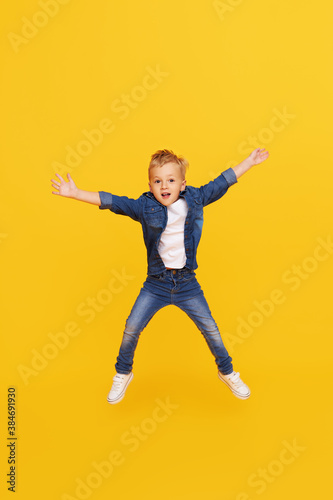 Full length portrait of excited little child boy Jumping for joy isolated on yellow background.