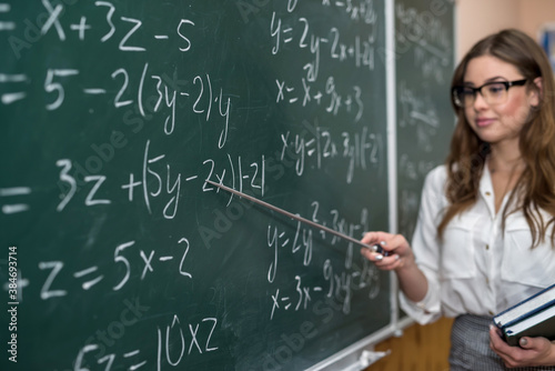 beautiful young teacher shows a pointer to the solution of math exercise in the classroom