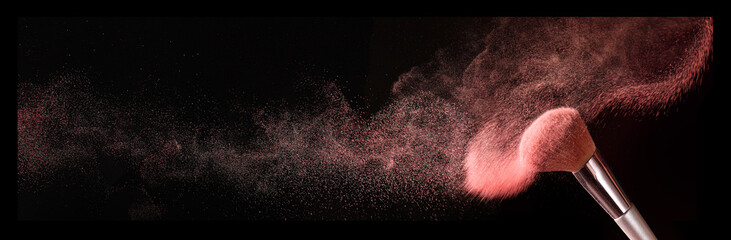 Makeup brush and burst of cosmetics on dark background