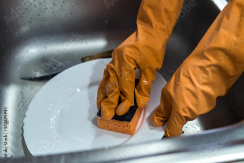 Female hand in gloves washing dishes over the sink in the kitchen