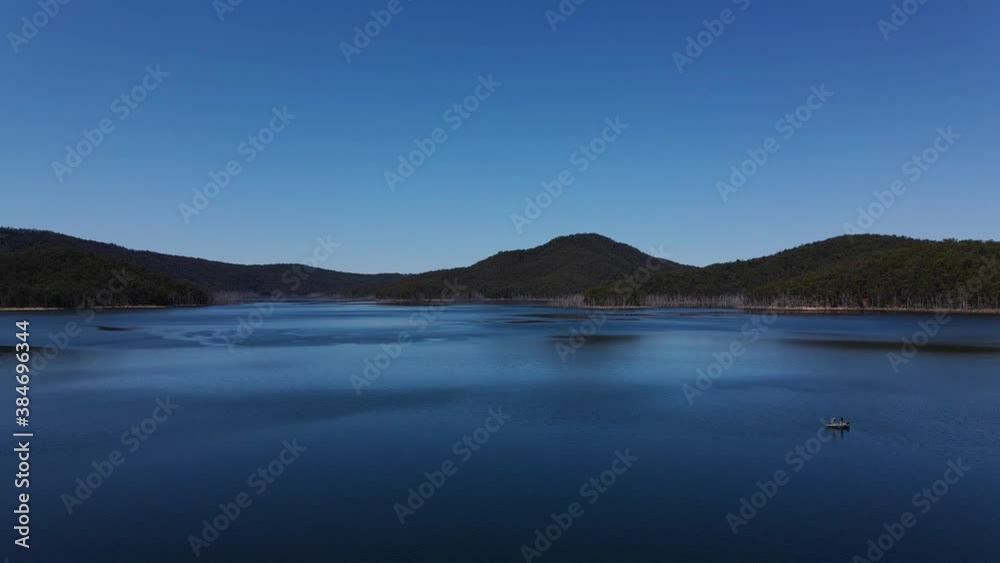 People On Boat Floating At The Calm Blue Waters Of Hinze Dam - Blue Sky Over The Mountains And Advancetown Lake - Gold Coast, QLD, Australia. - aerial ascending shot People On Boat Floating At The Calm Blue Waters Of Hinze Dam - Blue Sky Over The Mountains And Advancetown Lake - Gold Coast, QLD, Australia. - aerial ascending shot