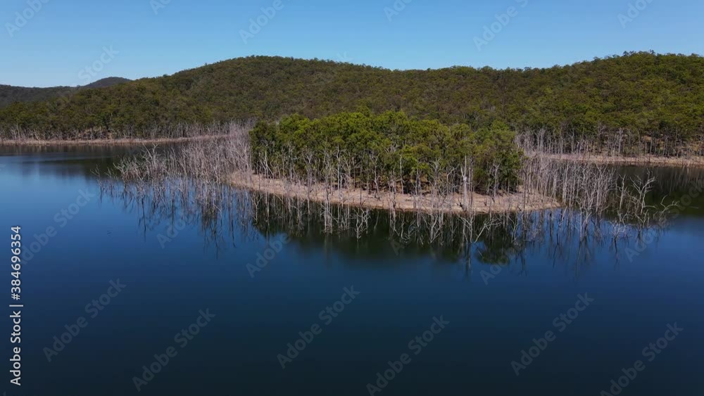 Dead Trees In Shallow Water Surrounding The Islet With Lush Trees - Hinze Dam And Advancetown Lake - Gold Coast, QLD, Australia. - aerial pullback, ascending shot Dead Trees In Shallow Water Surrounding The Islet With Lush Trees - Hinze Dam And Advancetown Lake - Gold Coast, QLD, Australia. - aerial pullback, ascending shot