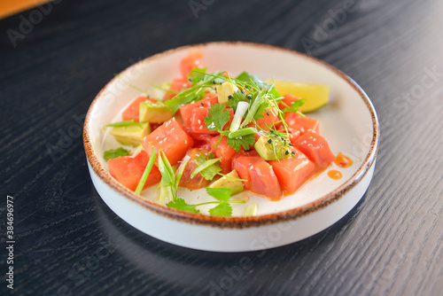 Watermelon salad with feta, fresh greenery and lime served in a unique shaped plate over black wooden table.