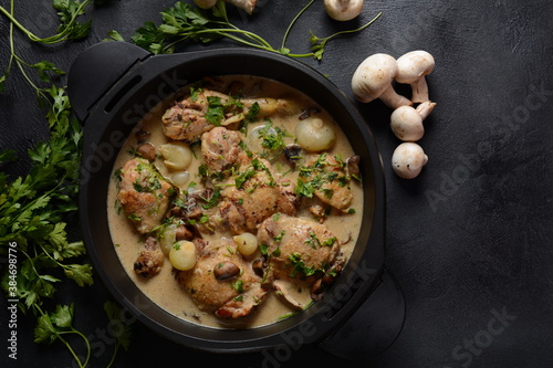 Fricassee - French Cuisine. Chicken stewed in a creamy sauce with mushrooms in a black dutch oven on a black table 