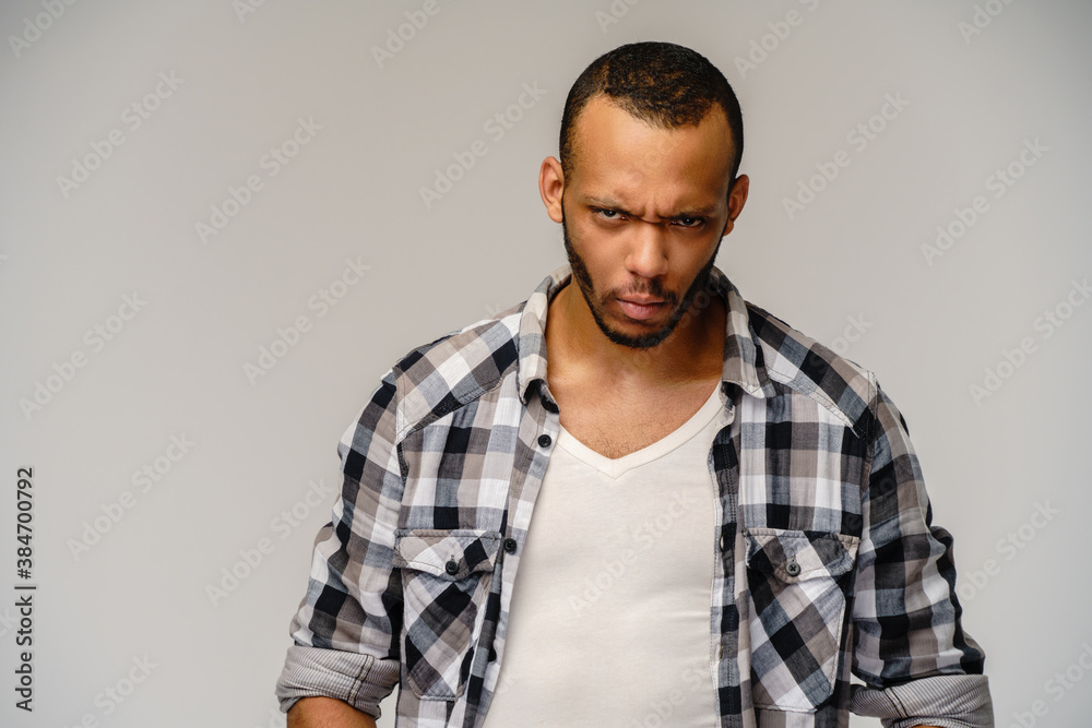 Photo of emotional angry sad young african-american man standing over light grey background Photo of emotional angry sad young african-american man standing over light grey background