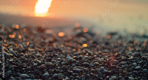 Fototapeta Naklejka Na Ścianę i Meble -  Close-up view of a pebble beach with blurred sea and sun background, selective focus
