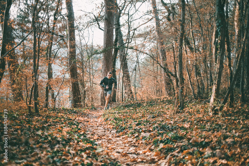 The concept of sports and cross-country running. A man in sports clothes runs along forest paths. The trunks of the trees in the background. Copy space © _KUBE_