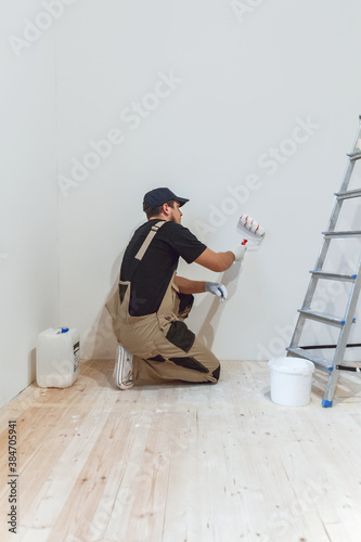 Obraz na płótnie Handsome painter with paint roller in empty room paints the wall