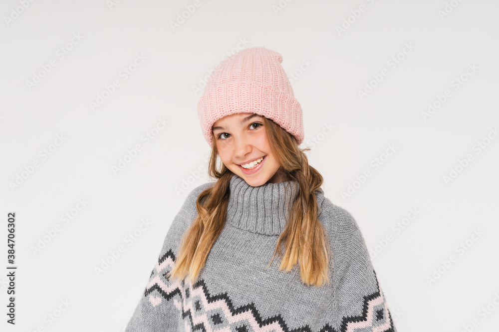 Cute smiling teenage girl in pink knitted hat and cozy gray poncho isolated on the white background