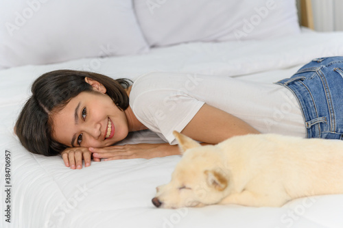 Young asian woman lying with white Shiba Inu puppy sleeping on white bed, Cheerful and nice couple with people and pet. Pet Lover concept