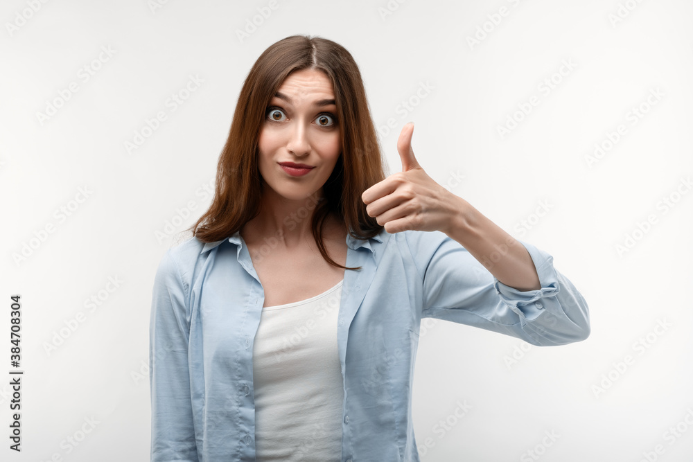 Portrait of cheerful young woman with long chestnut hair showing thumb up. Human emotions concept Portrait of cheerful young woman with long chestnut hair showing thumb up. Human emotions concept