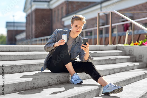 technology, communication and lifestyle concept - young man or teenage boy with non alcoholic drink in tin can using smartphone in city