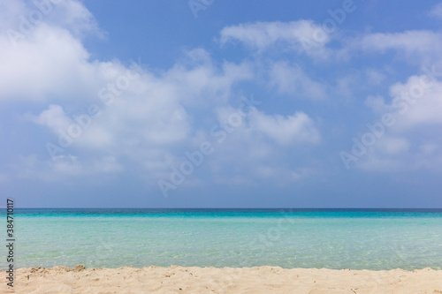 Looking out over a turquoise sea with sandy beach and a blue cloudy sky