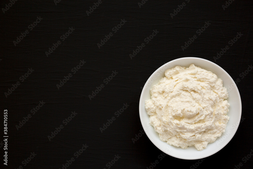 Tasty Ricotta Cheese in a white bowl on a black background, top view. Overhead, from above, flat lay. Copy space. Tasty Ricotta Cheese in a white bowl on a black background, top view. Overhead, from above, flat lay. Copy space.