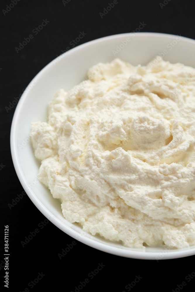 Tasty Ricotta Cheese in a white bowl on a black background, low angle view. Close-up.