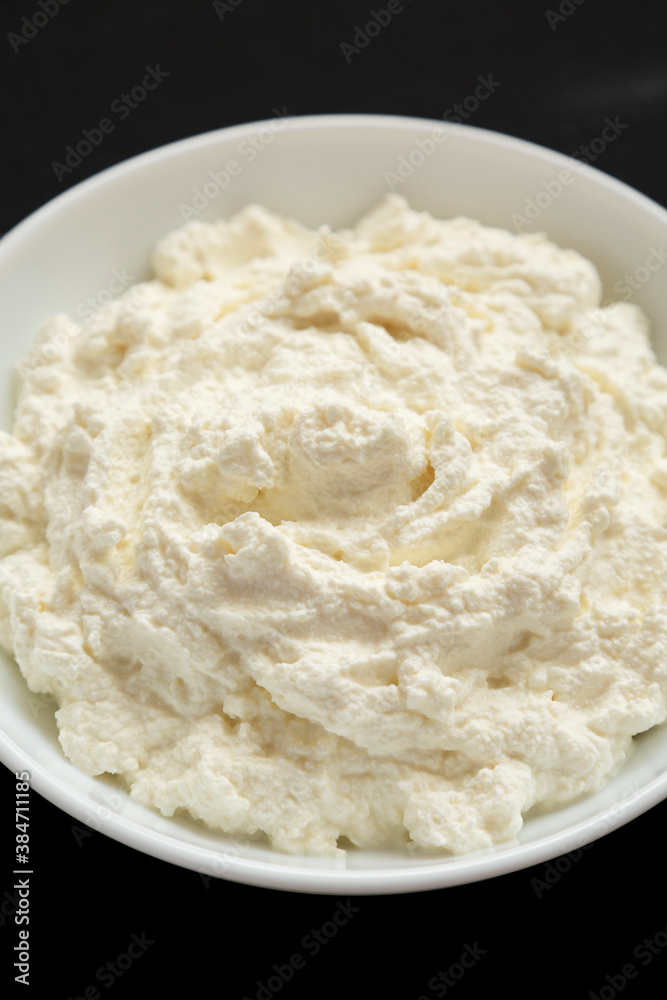 Tasty Ricotta Cheese in a white bowl on a black surface, side view. Close-up. Tasty Ricotta Cheese in a white bowl on a black surface, side view. Close-up.