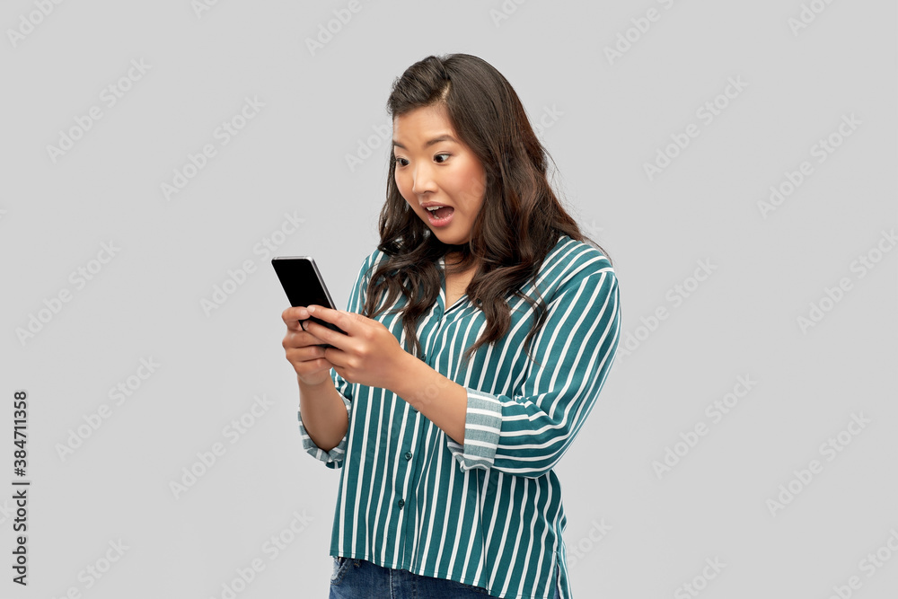 technology and people concept - surprised asian woman using smartphone over grey background technology and people concept - surprised asian woman using smartphone over grey background