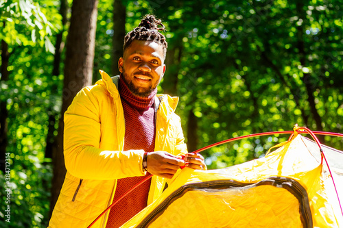 african american in yellow jacker putting on a tent in forest photo