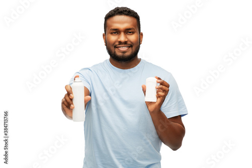 hygiene, grooming and people concept - happy smiling african american man choosing between stick deodorant and antiperspirant spray over white background