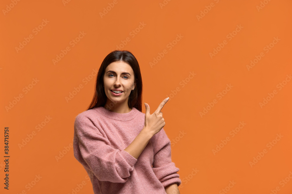 This is a good offer. Portrait of positive amazed dark head female pointing right, smiling with pleasure, glad to advise. wears in pink knitted sweater isolated over orange wall This is a good offer. Portrait of positive amazed dark head female pointing right, smiling with pleasure, glad to advise. wears in pink knitted sweater isolated over orange wall