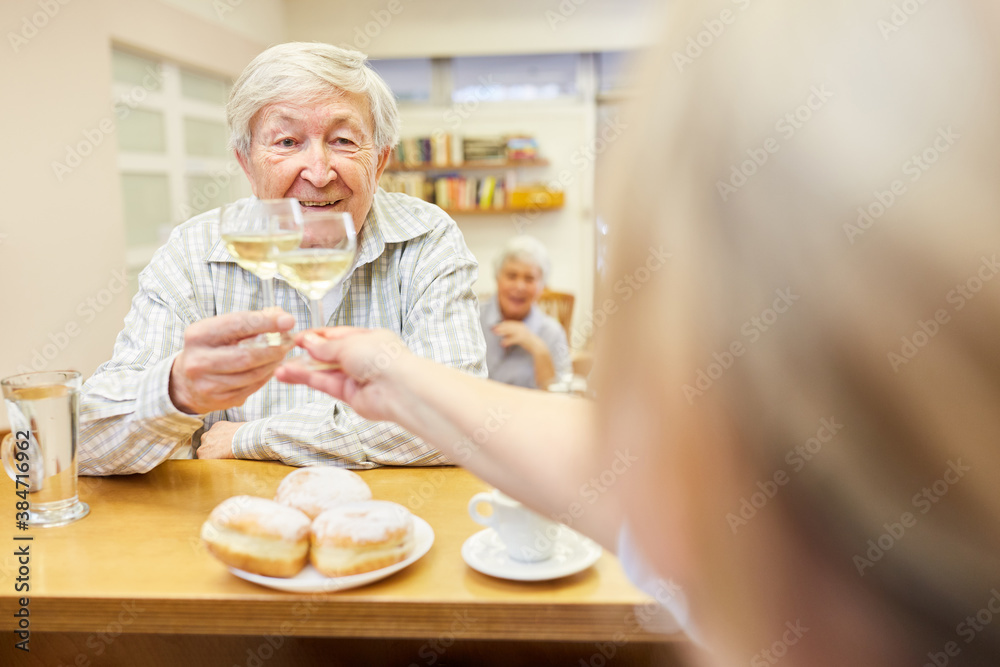 Senior beim Anstoßen mit einem Glas Weißwein im Aufenthaltsraum im Seniorenheim