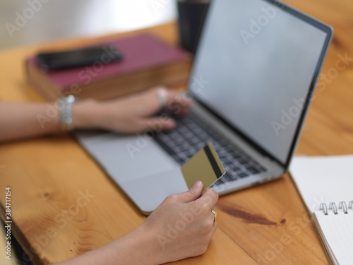 Female hand holding credit card and typing on mock up laptop to online payment