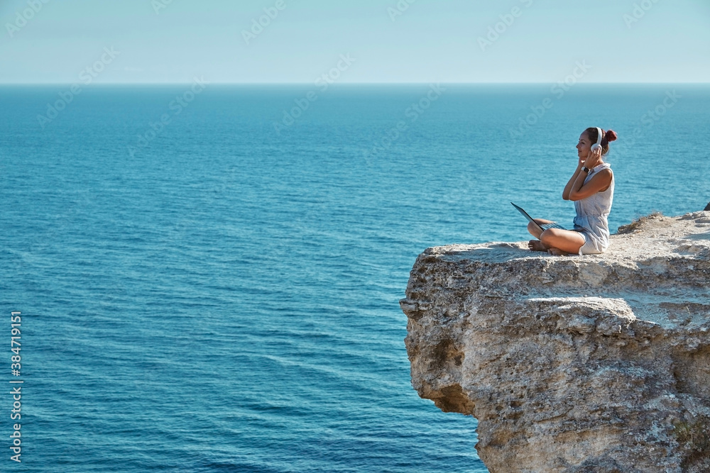 Freelance job travelling and remote office concept. Cheerful woman sitting on rock with laptop. Work from any country.
