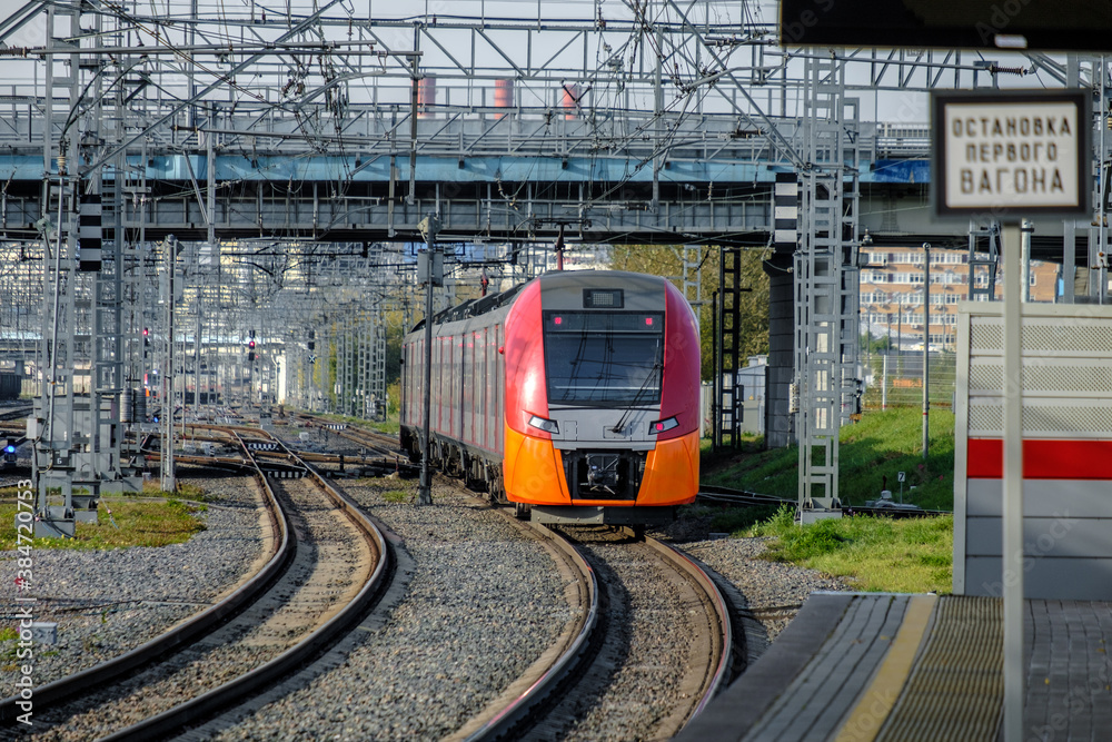Naklejka premium A modern high-speed red train on a section of the Moscow Central Circle Line. Comfortable city rail public transport. Summer sunny day. The inscription in Russian means: Stop of the first car.