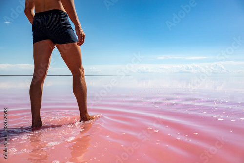 Fototapeta Naklejka Na Ścianę i Meble -  Man legs view walking in pink salt lake water with blue sky in vibrant colors. Spa recreation in summer on Syvash or Sivash, the Putrid Sea or Rotten Sea, Ukraine