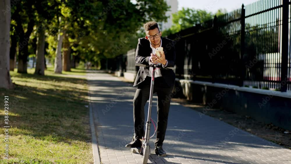 Good looking charismatic man Afro American office worker make a stop with his electric scooter in the middle of the street and have a conversation on his smartphone Good looking charismatic man Afro American office worker make a stop with his electric scooter in the middle of the street and have a conversation on his smartphone