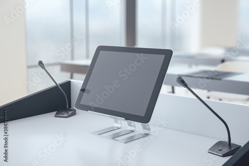 Rostrum with digital tablet and microphone in conference hall.