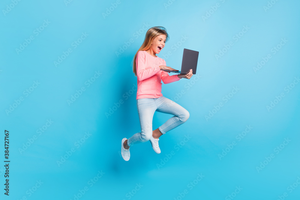 Photo portrait of laughing girl jumping up holding laptop isolated on pastel blue colored background Photo portrait of laughing girl jumping up holding laptop isolated on pastel blue colored background