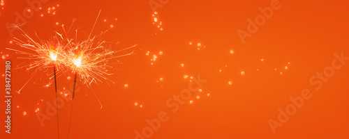 zwei brennden Wunderkerzen vor leuchtendem orange hintergrund, abstraktes modernes party konzept banner mit freiem textraum