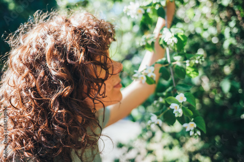 Portrait of young woman with curly hair enjoying scent of blooming tree flowers