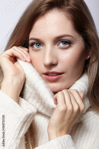 Blonde young beautiful woman dressed in white woolen sweater .