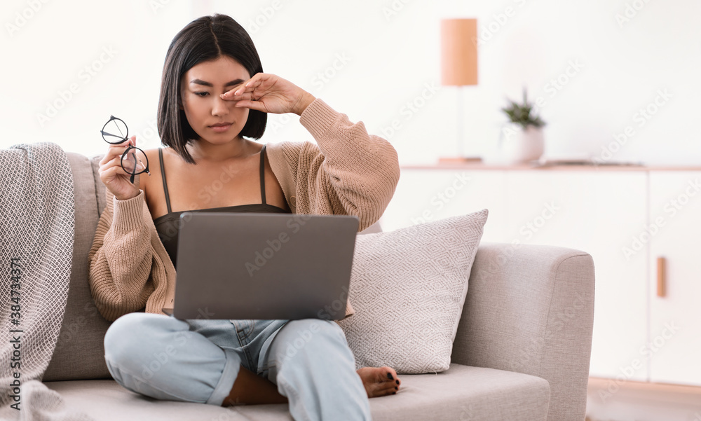 Naklejka premium Tired asian lady rubbing her eye using laptop