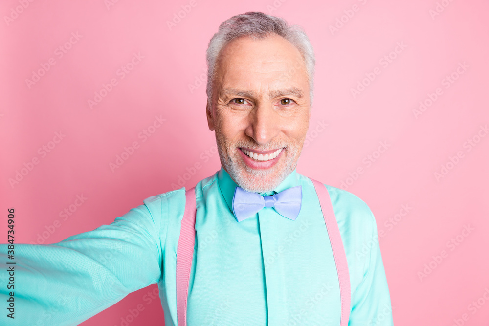 Close up photo portrait of old man looking at camera taking selfie suspenders bowtie isolated on pink color background Close up photo portrait of old man looking at camera taking selfie suspenders bowtie isolated on pink color background