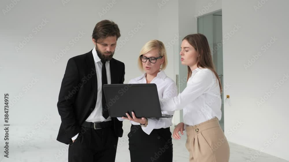Real estate agent shows the project of the apartment to a young couple on a laptop. Real estate agent shows the project of the apartment to a young couple on a laptop.