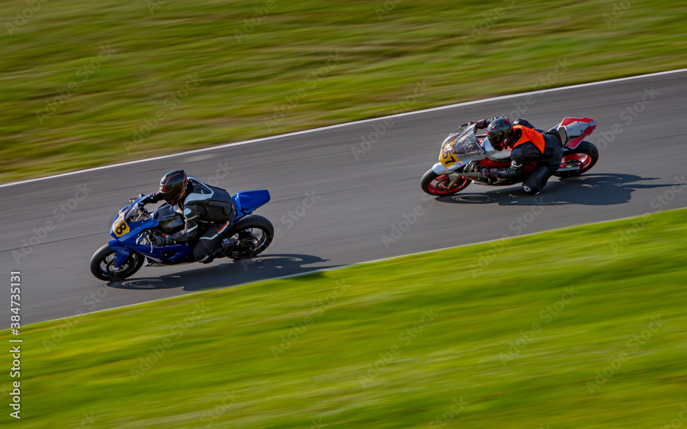 A panning shot of two racing bikes cornering as they circuit a track.