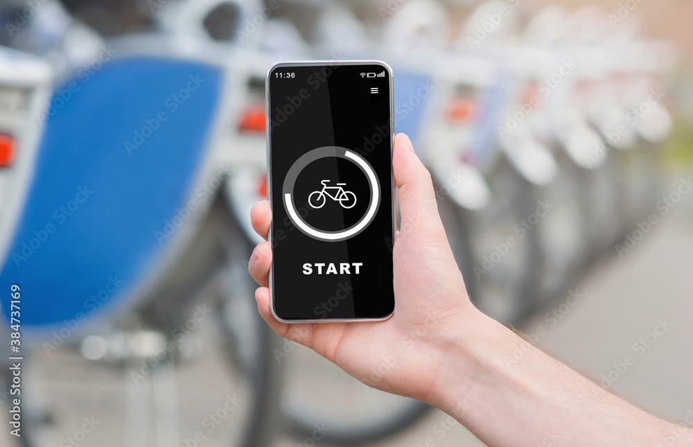 Modern outdoor workout with technology and bicycle trip. Hand holds phone with start button and bike on screen Modern outdoor workout with technology and bicycle trip. Hand holds phone with start button and bike on screen
