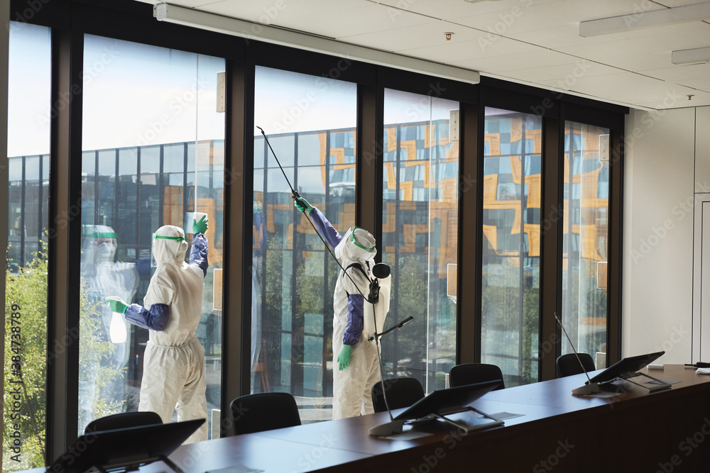 Wide angle portrait of two workers wearing hazmat suits disinfecting office windows in conference room, copy space - obrazy, fototapety, plakaty 