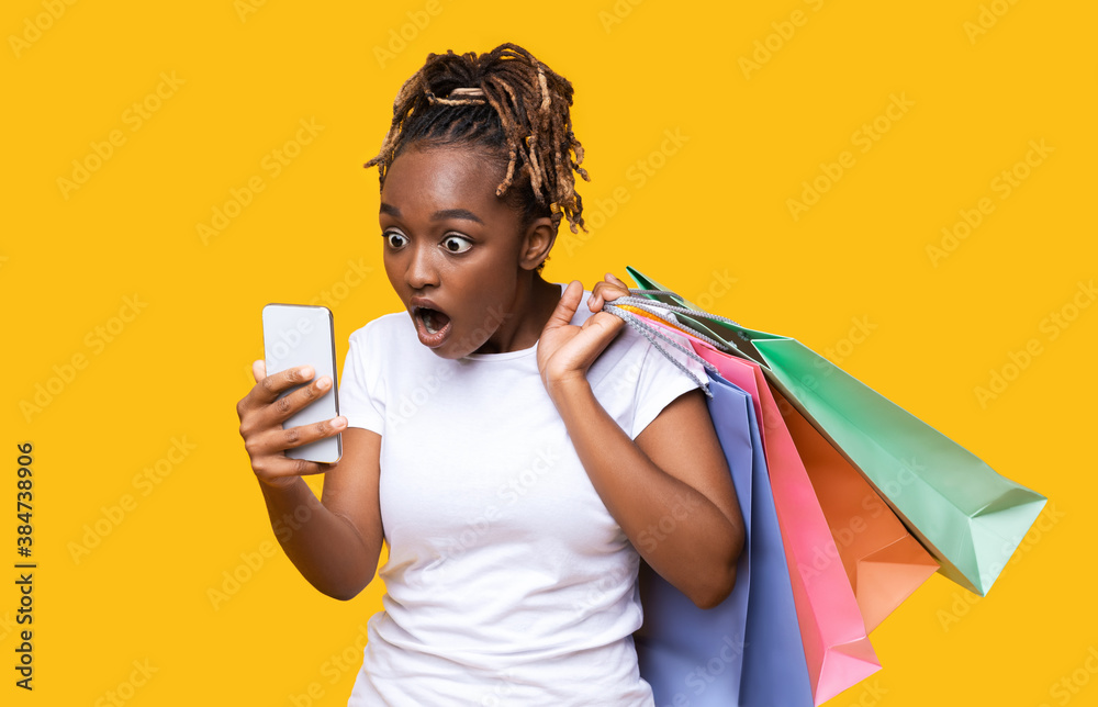 Amazed african woman with shopping bags looking at phone screen Amazed african woman with shopping bags looking at phone screen