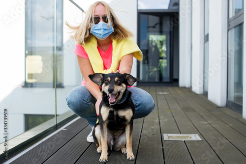 Young woman at home on a terrace with protective mask. Hugging her cute black dog. Corona virus Covid-19 concept. Quarantine theme. woman is not leaving home because of a pandemic. Lonely in illness.
