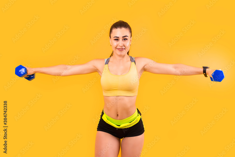fitness girl in yellow and black sportswear makes pumping hands exercise with dumbbells. sport concept photo. isolated on yellow background. copy space fitness girl in yellow and black sportswear makes pumping hands exercise with dumbbells. sport concept photo. isolated on yellow background. copy space