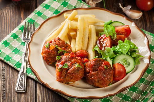 Roasted meatballs in tomato sauce with french fries and salad