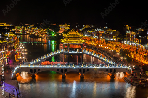 Beautiful night scenery and Fenghuang Bridge of Fenghuang (Phoenix) ancient town, Hunan province, China. Cityscape at night with reflection light in the river. © Thongchai S.