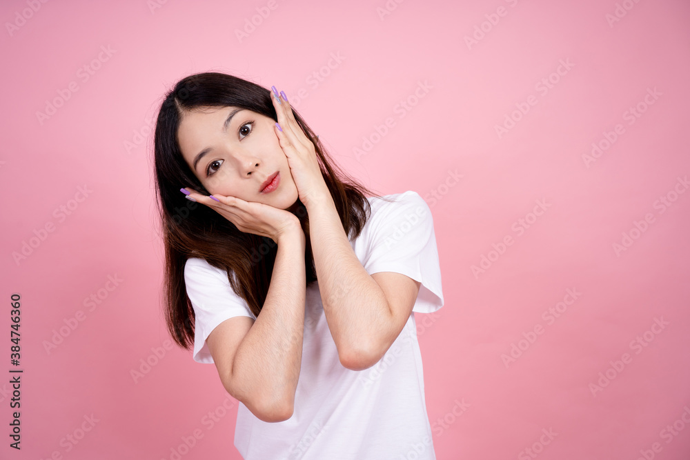 Beautiful Asian woman is smiling and she touches her cheek on a pink background. Beautiful Asian woman is smiling and she touches her cheek on a pink background.