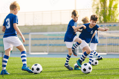 Young boys playing football training game. Happy children kicking soccer balls on practice pitch. Soccer training stadium in the background. School age boys in soccer blue jersey shirts © matimix