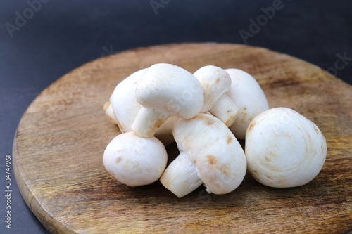 Whole Fresh white button mushrooms or Agaricus or champignon mushrooms on a rustic wooden chopping board. over black background. food Product photo with copy space.