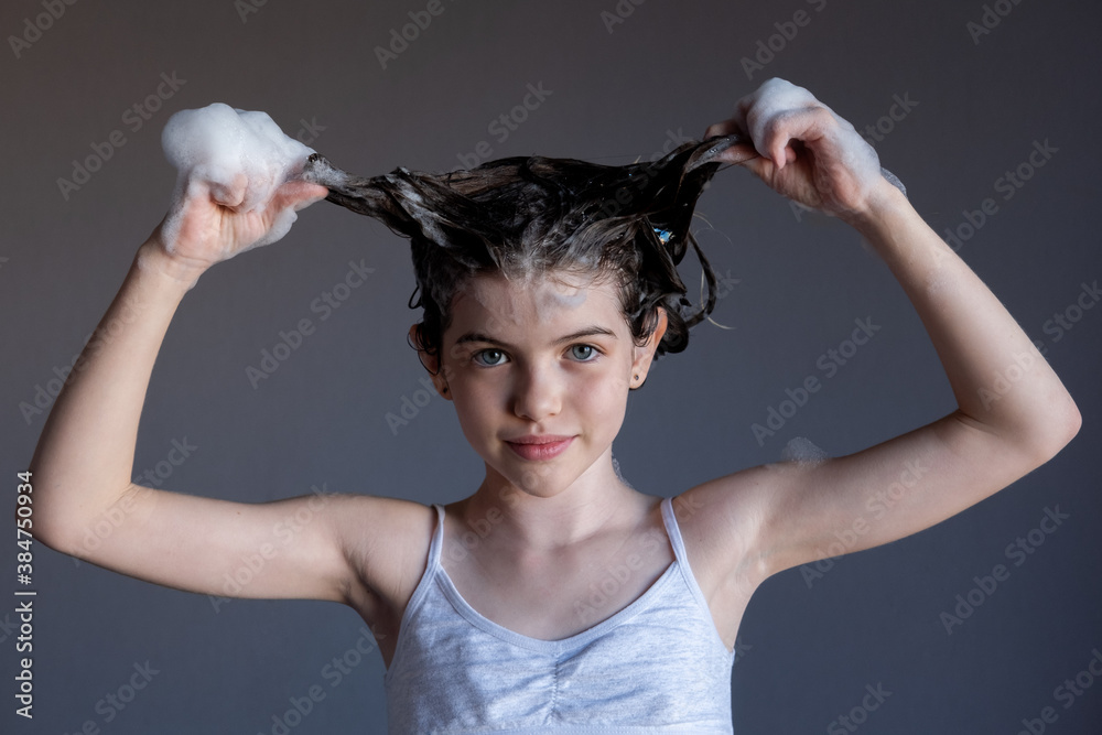 little / young girl washes her hair, soap suds from shampoo on her head, portrait. Child makes horns from hair